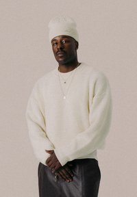 Elfenbensfarvet strikket sweater med ribbet krave og manchetter, parret med en matchende hue. Sølvhalskæder med vedhæng bæres.