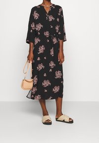 Musta kukkakirjailulla varustettu kietaisumekko, jossa on kolme neljäsosaa hihat, vyötärölle sidottava nauha ja polveen ulottuva helma. Yhdistetty beigen värisiin sandaaleihin ja pieneen ruskeaan laukkuun.