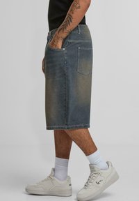 Denim midi skirt, light blue with faded finish, five-pocket design, belt loops, and straight cut. Paired with white sneakers and socks.