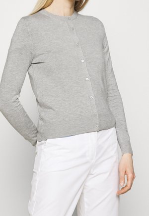 Lichtgrijze gebreide cardigan met een ronde halslijn, voorste knopen en geribbelde manchetten. Draagt over witte broeken met een gladde textuur.