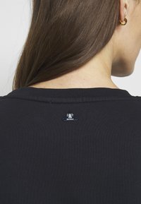 Černé ribbed tričko s kulatým výstřihem. Na zadní straně poblíž límce se nachází malá nášivka s logem majáku a textem "Barbour".