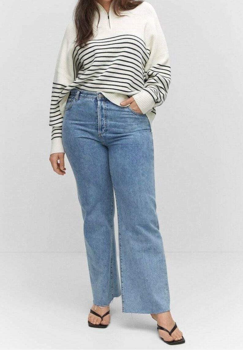 Kremowy i czarny sweter w paski z długim rękawem i wysokim kołnierzem, w połączeniu z jasnoniebieskimi szerokimi jeansami i czarnymi sandałami na ramiączkach.