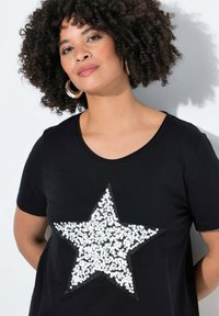 Zwarte T-shirt met korte mouwen, voorzien van een groot witte paillettensterontwerp. Zachte stof met een gladde textuur en een ronde halslijn.