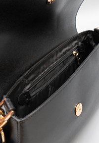 Interno di borsa nera in pelle con tasca con zip e fodera testurizzata. Accessori in metallo color oro impreziosiscono l'esterno.