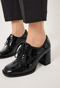 Scarpe stringate in pelle verniciata nera con punta quadrata e tacco chunky. Presentano cuciture dettagliate e lacci neri.