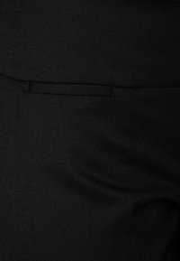 Zwarte stoffen broek met een gladde textuur, een zijzak en subtiele details. De stof is gestructureerd en op maat gemaakt.