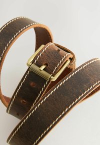 Bruine leren riem met witte stiksels, voorzien van een gestructureerde gesp van goudkleurig metaal en meerdere verstelgaten.