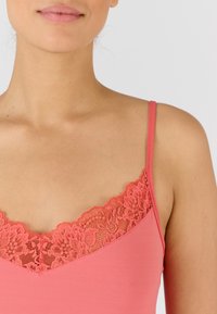 Canotta rosa con sottili spalline e un colletto in pizzo. Il tessuto è liscio ed elastico, con una forma aderente.