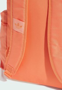 Orange ryggsäck i slitstarkt tyg, med en sidoficka, justerbar axelrem och en logopatch med tre ränder design.