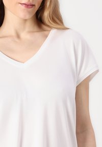 Hvit V-hals t-skjorte med korte ermer, laget av glatt stoff, med et minimalistisk design og en avslappet passform.