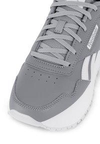 Záber zblízka na šedé a biele tenisky Reebok s šnúrkami, sieťovaným jazykom, perforovanou špičkou a viditeľným logom značky na boku.