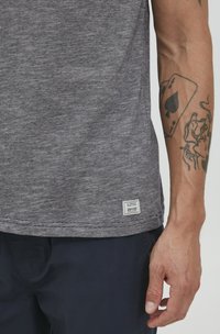 Šedé vřesové tričko s kulatým výstřihem, krátkými rukávy a malou značkovou visačkou na dolním lemu. Tkanina vypadá měkce a strukturovaně.