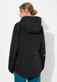 Chaqueta negra aislante con capucha, que presenta un acabado acolchado, mangas de largo completo y acentos reflectantes en los puños.