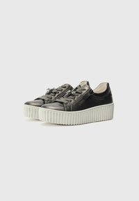 Sorte lærplatformsneakers med en ribbet hvid sål, der har dekorative snørebånd og blomsterdekorationer på forsiden.