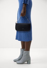 Black leather clutch with silver chain strap, smooth texture, rectangular shape. Paired with light blue ankle boots and a ribbed blue dress.