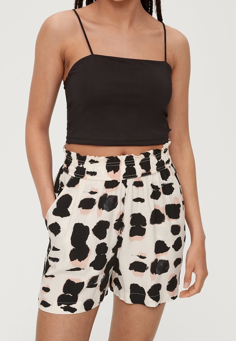 Black cropped tank top with thin straps paired with loose, cream shorts featuring a black and pink abstract print and elastic waistband.