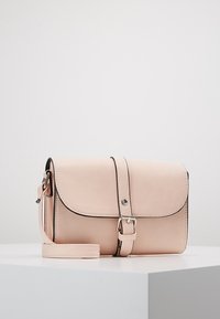 Blush pink lædertaske med en struktureret form, magnetisk flaplukning og justerbar rem, med enkle sorte syninger som accent.