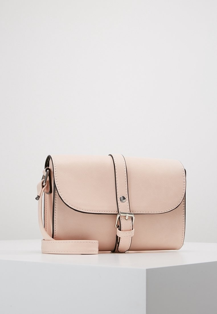 Blush pink lædertaske med en struktureret form, magnetisk flaplukning og justerbar rem, med enkle sorte syninger som accent.