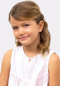 Pige med mellemlangt, bølget brunt hår iført en lyserød ærmeløs kjole med en samlet design og en vedhængs necklace med en flamingo charm.