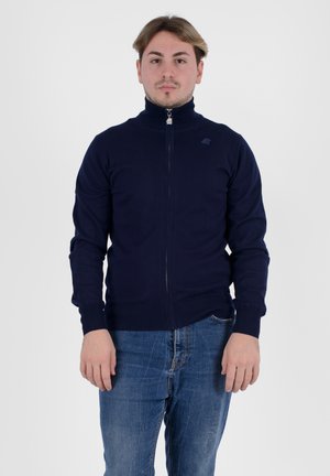 Maglione zip-up blu navy realizzato in tessuto testurizzato con colletto alto. Presenta polsini e orlo a costine, con un piccolo logo sul petto.