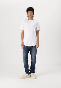 T-shirt en coton blanc, jeans en denim bleu et baskets beiges. Coupe droite avec des manches courtes et un col rond. Style minimaliste.