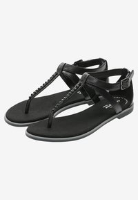 Sandali piatti neri con design a sandalo e cinturini testurizzati e una piccola fibbia. Materiale morbido con suola piatta, adatti per un uso casual.