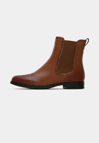 Brown leather ankle boots with elastic side panels, decorative perforations at the toe, and a low black heel. Smooth texture and classic design.