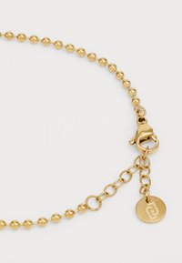 Collana in oro con catena e perle sferiche, chiusura a granchio e un piccolo pendente con logo. Texture liscia e finitura lucida.