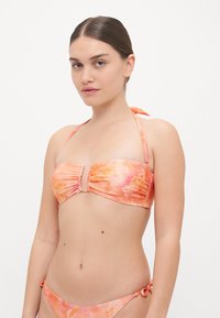 Bikini with a bandeau top featuring ruching and a front clasp, in varying shades of pink with floral patterns. Ties at the neck and sides.