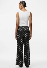 Balta bez piedurknēm blūze, kas kombinēta ar brīviem melniem biksēm ar baltām punktiņām, elastīgu jostasvietu un plaša kāju dizainu.