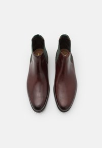 Botines de cuero marrón con paneles laterales elásticos verdes, punta afilada y textura suave. Diseñados para una apariencia elegante y ceñida.