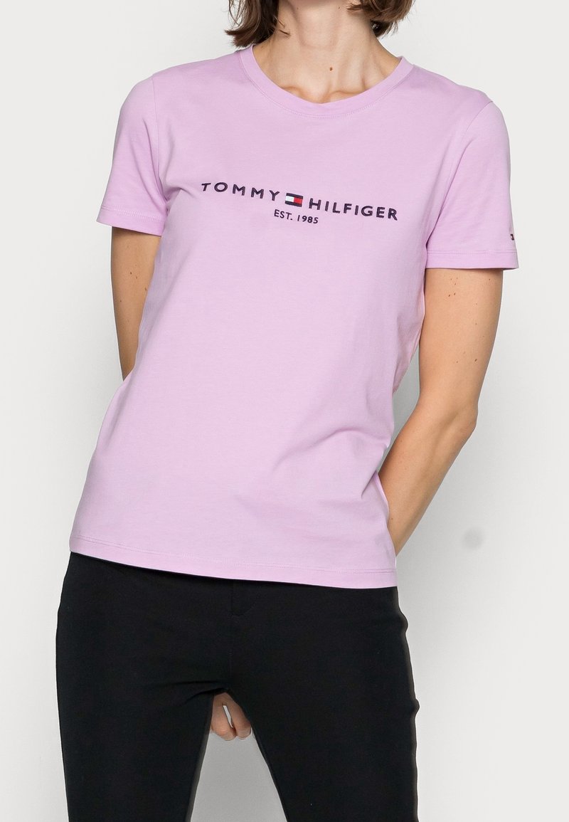 Ljuslila t-shirt med kort ärm i bomull, med en logotyp som har "TOMMY HILFIGER" och "EST. 1985" i mörk text. Klassisk rundhalsad design.