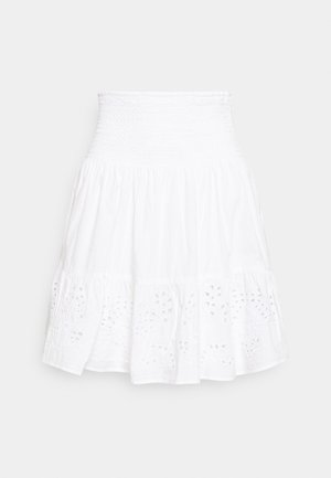 Witte knielange rok met brede geplooide tailleband en geborduurde eyelet bloemmotieven langs de zoom, plat uitgestald op lichte achtergrond.