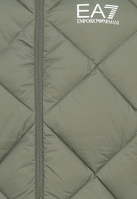 Lagani puffer jakna maslinaste boje s kvadratnim dijamantskim uzorkom i punim zatvaračem. Sadrži EA7 Emporio Armani logo u bijeloj boji.