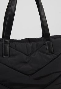 Sac en toile rembourré noir avec de larges poignées en cuir noir et un détail de piqure en chevron.