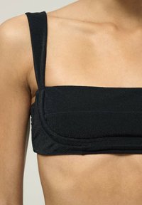Juoda bandeau liemenėlė su plačiomis petnešomis, tekstūruota medžiaga ir struktūrizuota dizainu, apimančiu raukšlėtą detalę priekyje.