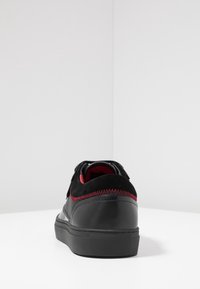 Czarne skórzane i zamszowe sneakersy z czerwonymi przeszyciami, okrągły dziób, płaska podeszwa i wyściełany kołnierz. Prosty czarny design, minimalne oznakowanie.