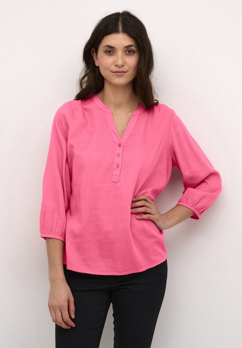 Blouse en lin rose avec un col en V et une patte de boutonnage à trois boutons. Dispose de manches trois-quarts avec des poignets élastiques et d'une coupe décontractée.