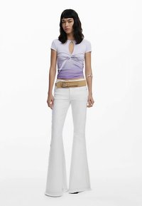 Violetti ombre -lyhythihainen paita, jossa on kierretty etuosan yksityiskohta, yhdistettynä valkoisiin levenevään lahkeiseen housuihin, joissa on sivusaumaukset ja leveä beige vyö.