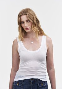 Camiseta de algodón blanca sin mangas con escote redondeado y tirantes finos. Combinada con unos vaqueros de mezclilla azules. Textura suave, diseño ajustado. Estilo sencillo.