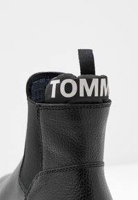 Czarne skórzane botki do kostki z elastycznymi bokami, teksturowanym wykończeniem i czarną pętelką oznaczoną napisem "TOMMY" w białym kolorze.