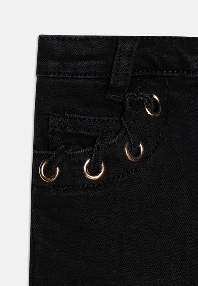 Détails d'un jean en denim noir avec une petite poche dotée d'un œillet, cousue avec du tissu noir. La texture est lisse et légèrement extensible.