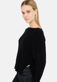 Maglione nero oversize con scollo rotondo e texture a coste, caratterizzato da un orlo asimmetrico e un accento di perle sul lato.