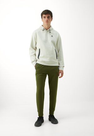 Haut en coton gris clair avec des accents noirs et des poches zippées, associé à un pantalon fuselé vert olive et des chaussures de sport noires.