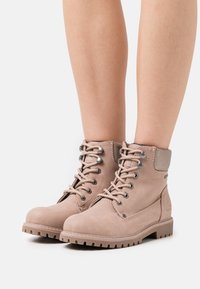 Bottines marron en daim avec une semelle robuste, bout rond et œillets en métal. Elles possèdent un col rembourré et des détails de couture.