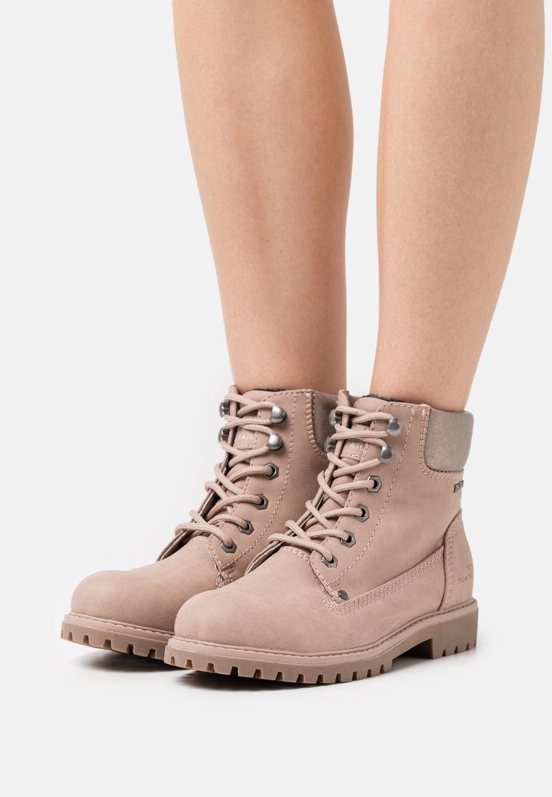 Bottines marron en daim avec une semelle robuste, bout rond et œillets en métal. Elles possèdent un col rembourré et des détails de couture.