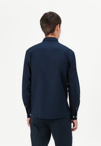 Camicia blu marina a maniche lunghe in misto cotone, colletto con bottoni, texture liscia, con bottoni ai polsini e orlo dritto.