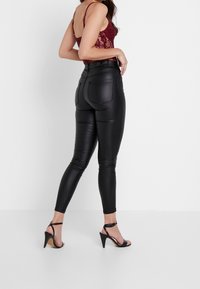 Black faux leather leggings with a fitted design, high waist, and back pockets, paired with a burgundy lace top and black heeled sandals.