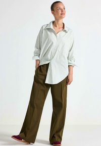 Oversized skjorte med grønne og hvide striber, kombineret med løstsiddende olivengrønne bukser og lilla slip-on sko.