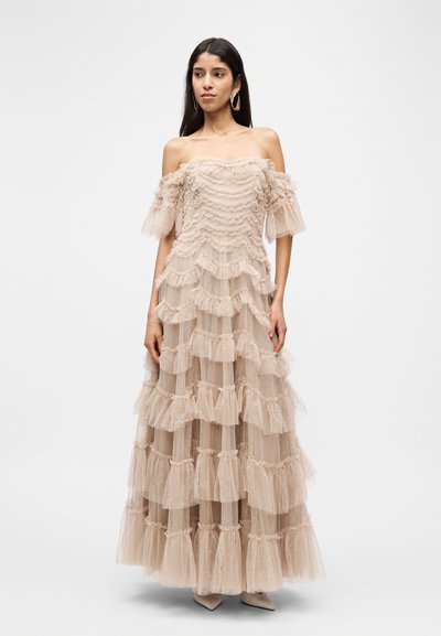 Schulterfreies, mehrlagiges Maxikleid aus leichtem beigen Tüll, mit gerafften Lagen und durchscheinender Textur. Kombiniert mit passenden spitzen Absatzschuhen.